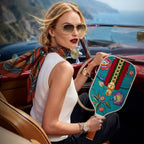 A luxury lifestyle shot of a fashion model holding a teal designer floral pickleball paddle while sitting in a vintage convertible car.